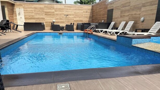 Et rektangulært swimmingpool med flisekant, omgivet af liggestole og en træterrasse.
