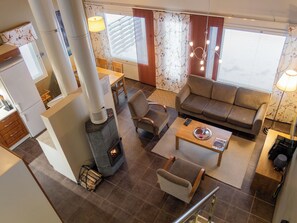 A modern living room with a fireplace, sofa, armchair, and a dining area with a table and chairs.