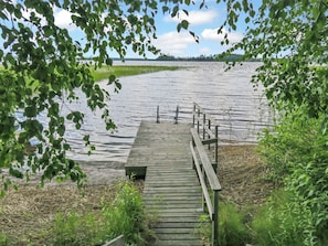 Une jetée en bois qui mène à un lac paisible, entouré de verdure et d’arbres.