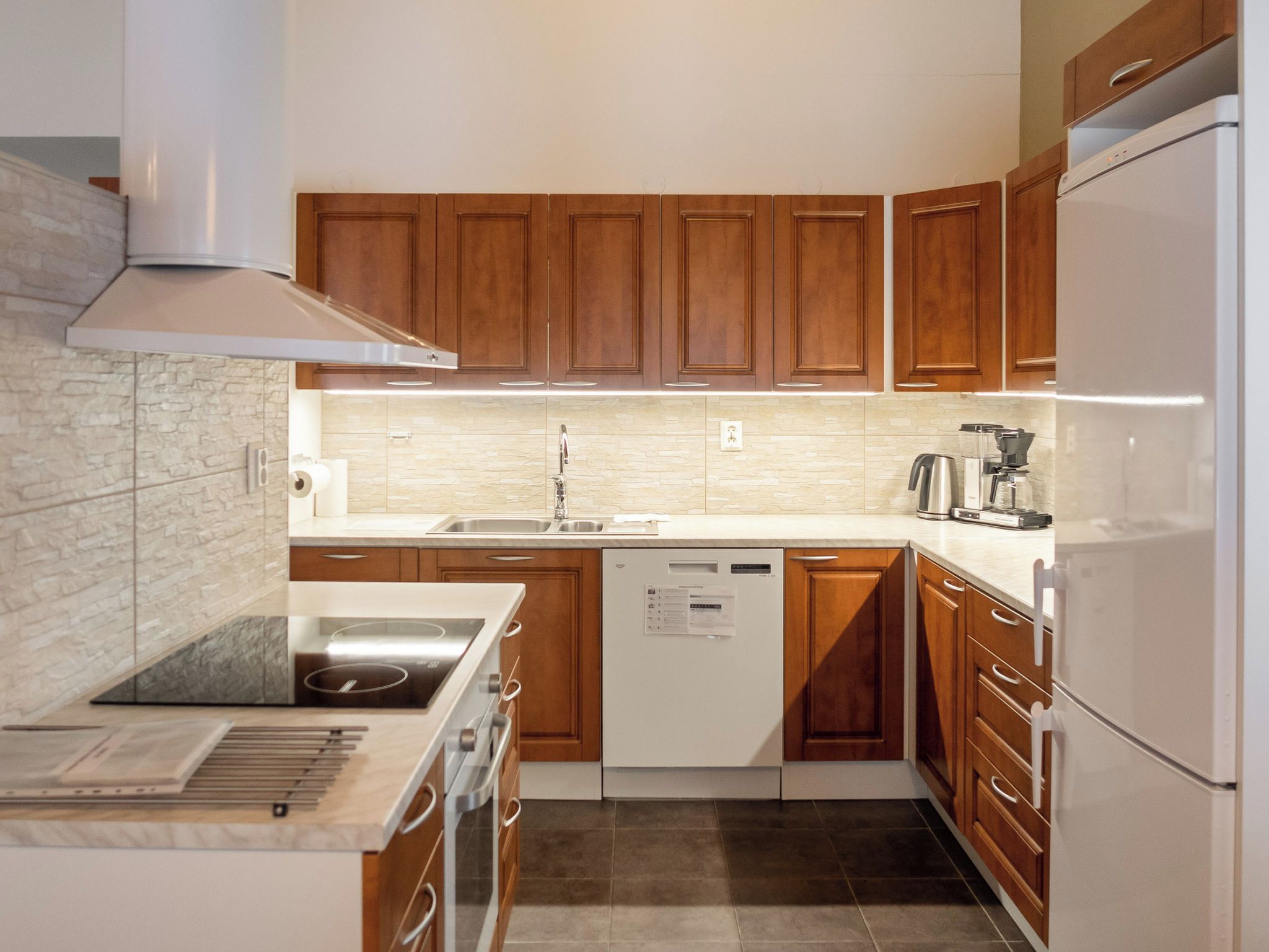 Eine moderne Küche mit Holzschränken, einem eingebauten Geschirrspüler und einer Edelstahl-Dunstabzugshaube.