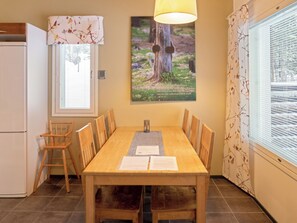 A dining area with a wooden table, chairs, a window with blinds, a lamp, and a framed picture on the wall.