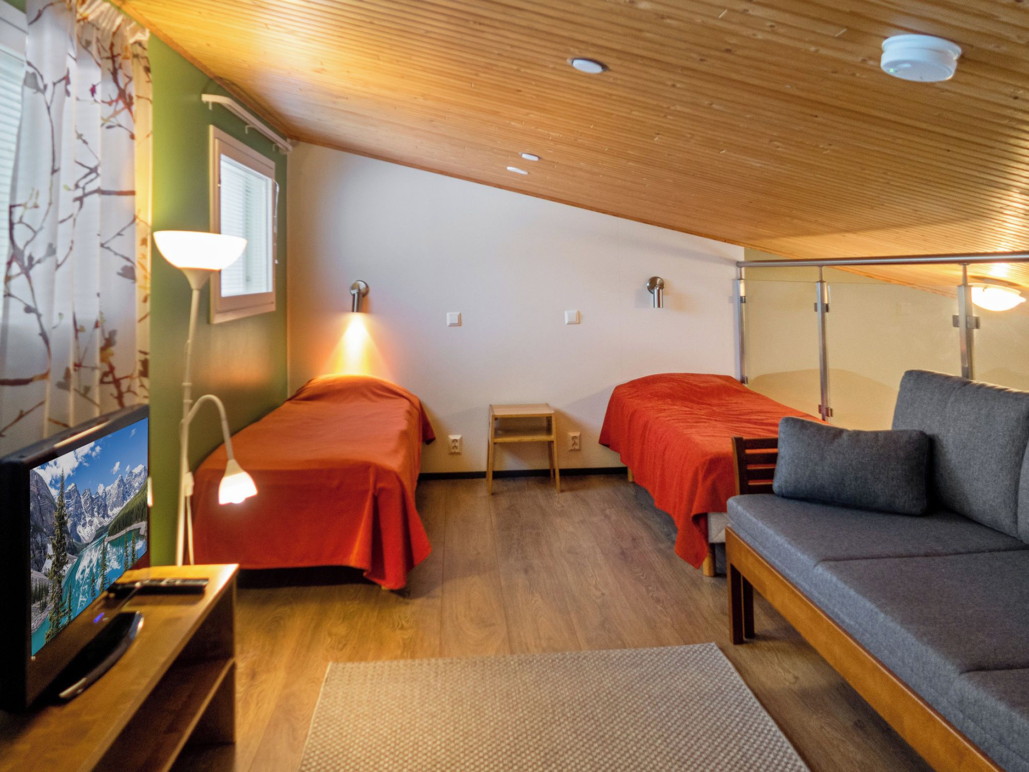 A room with two beds, a sofa, a TV, and a lamp.