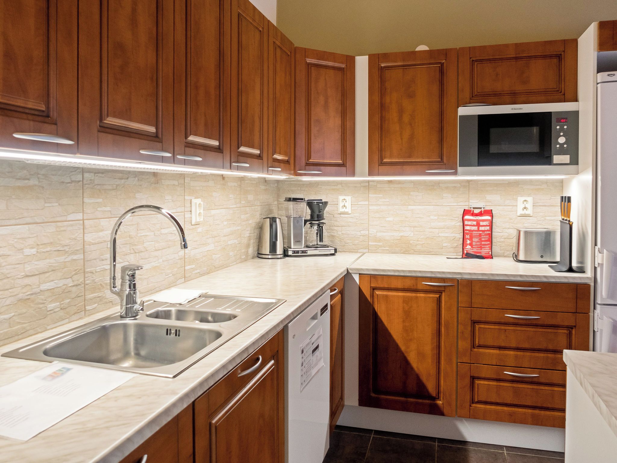 A modern kitchen with wooden cabinets, stainless steel appliances, and a stone backsplash.