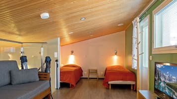 A compact room with a wooden ceiling, two beds with red bedding, a grey sofa, a small table, and a television on a wooden stand.