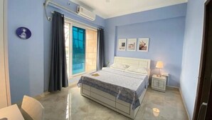 Een slaapkamer met een bed, nachtkastje, plafondventilator, raam met gordijnen en een wandairconditioner.