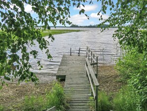 Un muelle de madera que conduce a un lago tranquilo, rodeado de follaje y árboles.