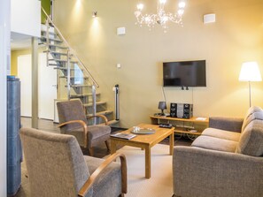 A modern living room with a flat-screen TV, comfortable seating, a staircase, and a chandelier. - Vuokatinranta suite 2 b by Interhome (Sotkamo)