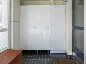 Ein kleiner, abgeschlossener Waschraum mit einer weißen Waschmaschine, einer hölzernen Sitzbank und einem gefliesten Boden.