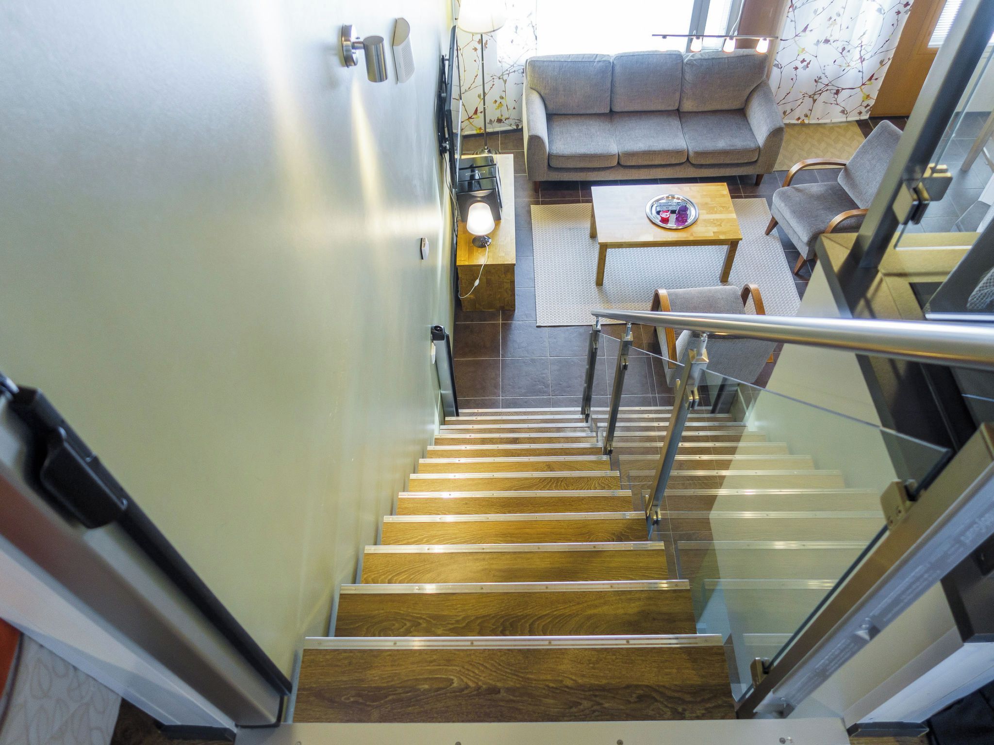 Un escalier avec des marches en bois et des rampes en métal mène à un espace de vie comprenant un canapé et une table.