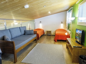Habitación compacta con sofá, dos camas individuales, una mesita, televisión y un cubo de basura.