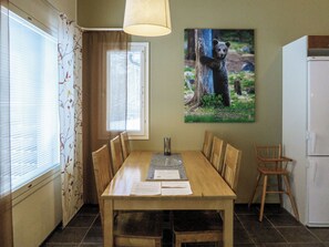 A dining area with a wooden table, chairs, a lamp, a framed picture, and a refrigerator.