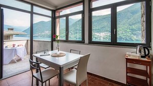 En balkon med et bord og stole, en vase med blomster, og udsigt til et bjergrigt landskab.