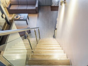 Un escalier avec des marches en bois et des rampes en métal mène à un espace de vie comprenant un canapé et une table basse.