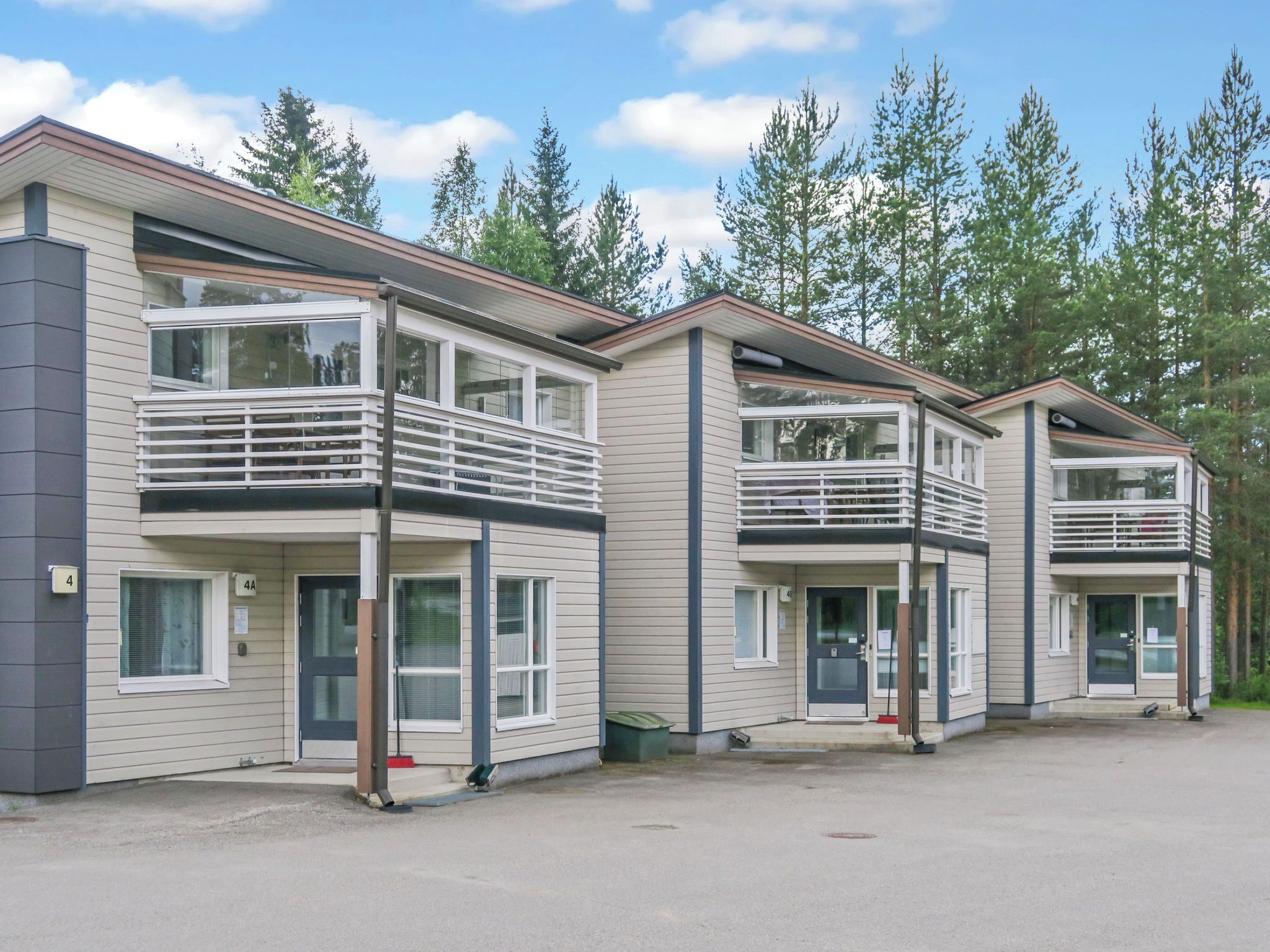 A row of modern multi-story buildings with balconies, large windows, and a parking area.