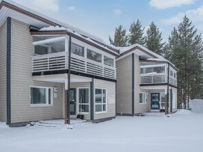 A modern two-story residential building with a balcony on the upper floor, a visible door labeled '4B', and a snow-covered ground.