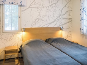 A single bed with a wooden headboard in a room with a window and a wall with a tree branch pattern.