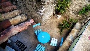 A patio area with a round blue table and blue chairs, surrounded by potted plants and a stone wall. - In the characteristic village of Bissone (Casa In Contrada) (Bissone)