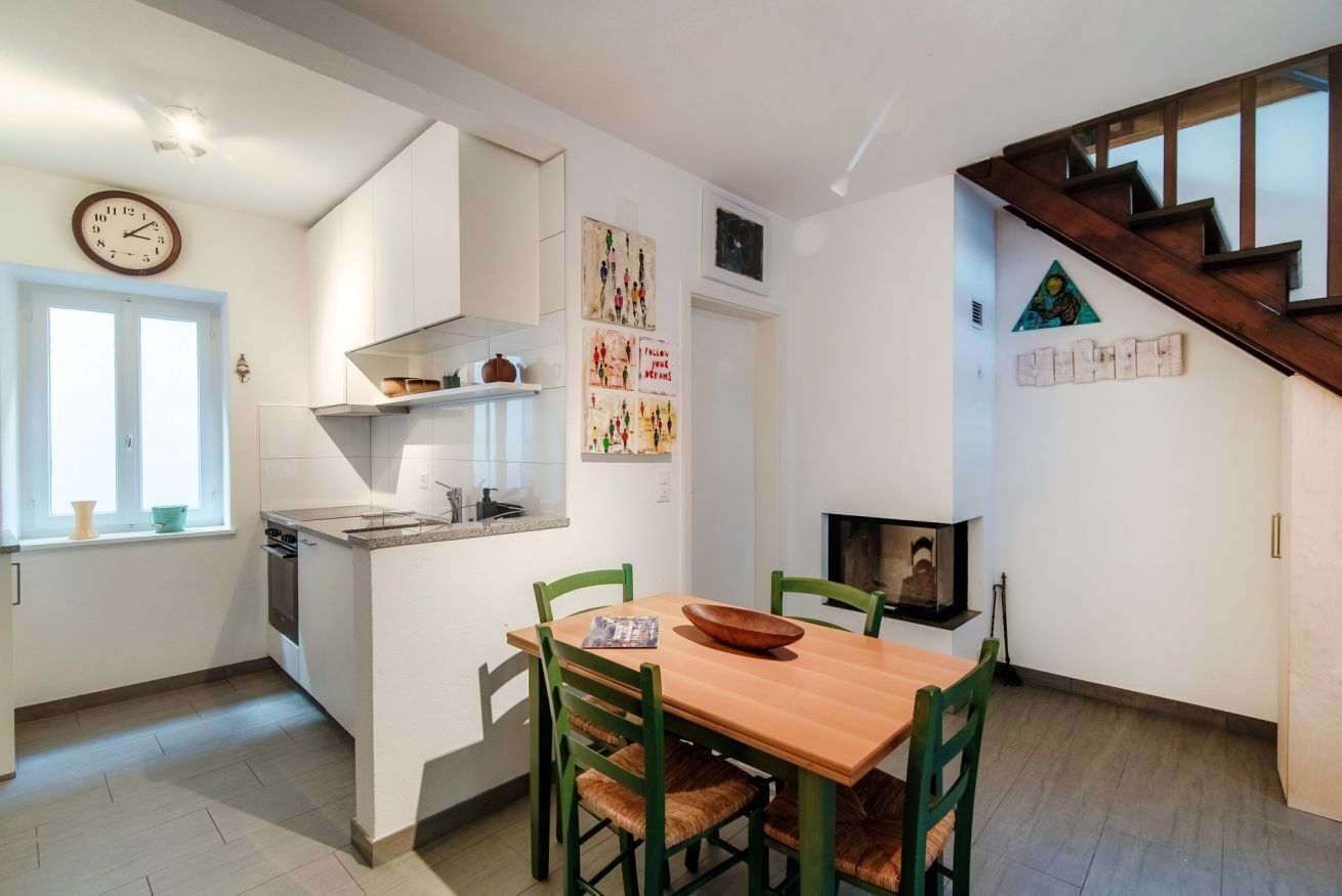 Une cuisine moderne avec des meubles blancs, une table à manger en bois et des chaises vertes. Il y a une horloge au mur et des œuvres d’art au-dessus des meubles.