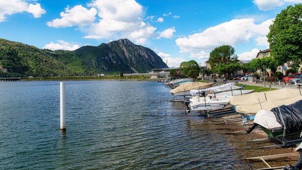 A lakeside view with boats docked, a mountain in the background, and a clear sky. - In the characteristic village of Bissone (Casa In Contrada) (Bissone)