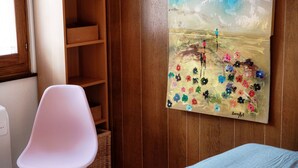 A room with a wooden wall, a white chair, a bed with a blue bedspread, and a painting of flowers and a landscape. - In the characteristic village of Bissone (Casa In Contrada) (Bissone)