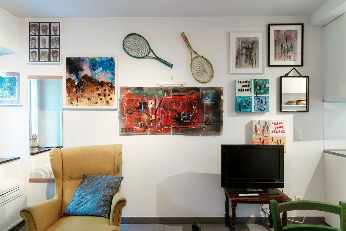 Un soggiorno con una poltrona beige, una televisione a schermo piatto e diverse opere d'arte alle pareti.
