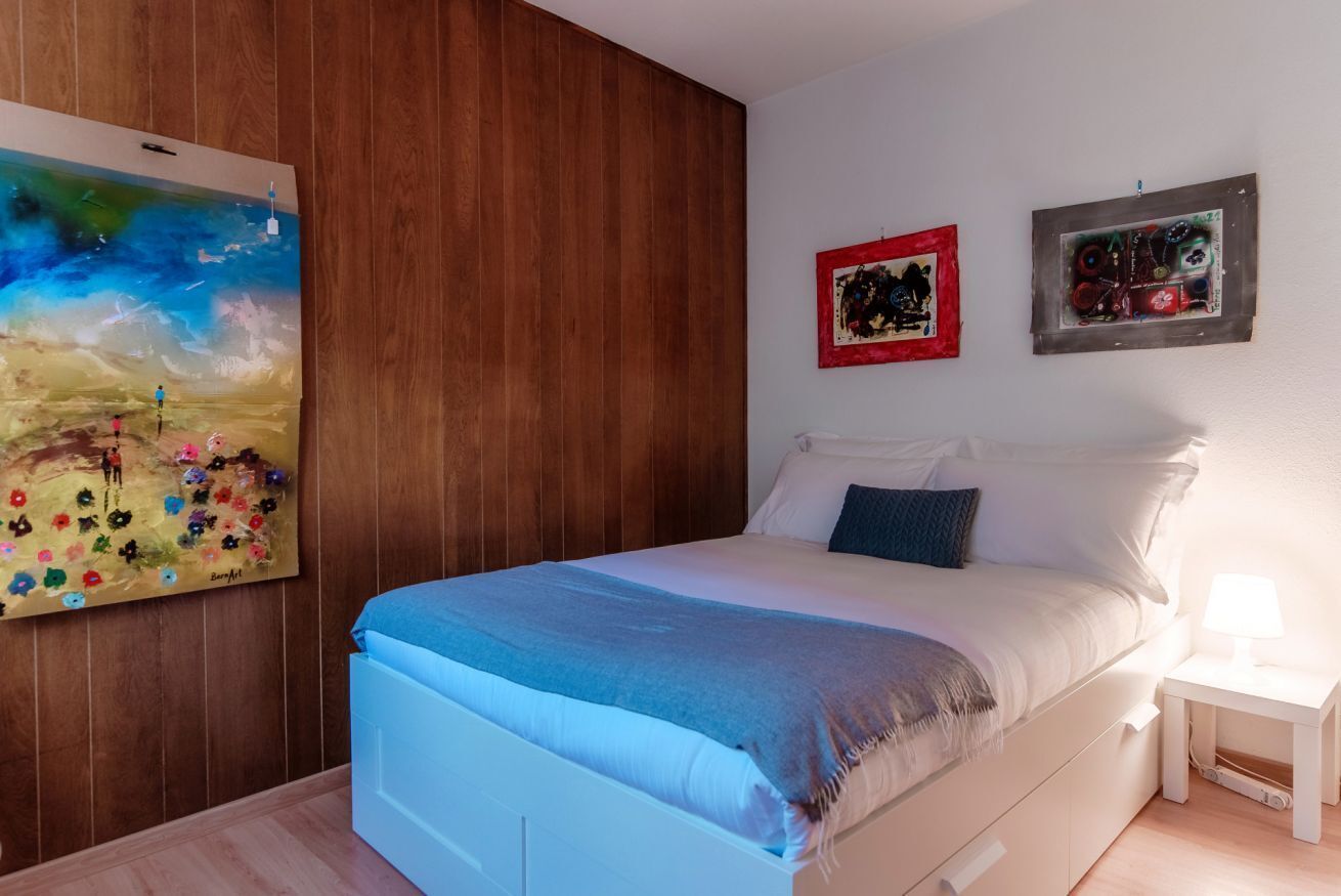 A bedroom with a bed, a nightstand, and a wall-mounted painting.