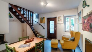 A dining area with a wooden table and chairs, a staircase, a yellow armchair, and a door leading to another room. - In the characteristic village of Bissone (Casa In Contrada) (Bissone)