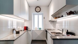 A modern kitchen with white cabinetry, a clock on the wall, and a window with a view. - In the characteristic village of Bissone (Casa In Contrada) (Bissone)