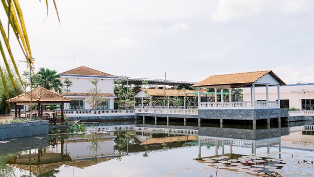 A serene hotel with a water feature in the foreground, a covered outdoor area, and a bridge connecting different sections of the property. - Ngoc Thu Hotel (Can Tho)