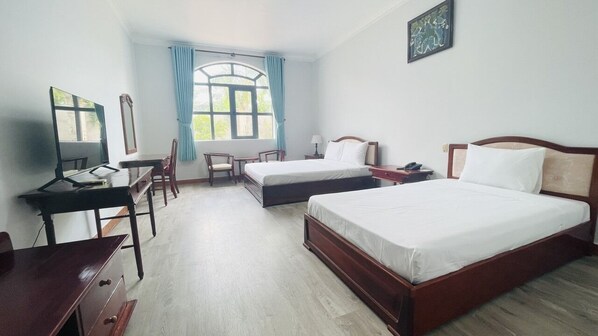Une chambre d’hôtel avec deux lits simples, un bureau avec une chaise, une petite table et une fenêtre avec des rideaux.