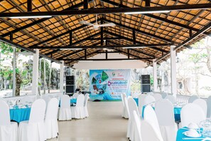 An indoor event space with white chairs and tables, a banner, and a thatched roof.