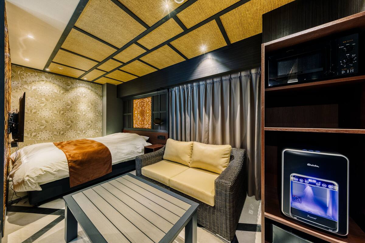 A modern hotel room with a bed, sofa, and a flat-screen TV on a stand.