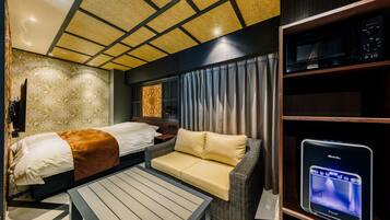 A modern hotel room with a bed, sofa, and a flat-screen TV on a stand.