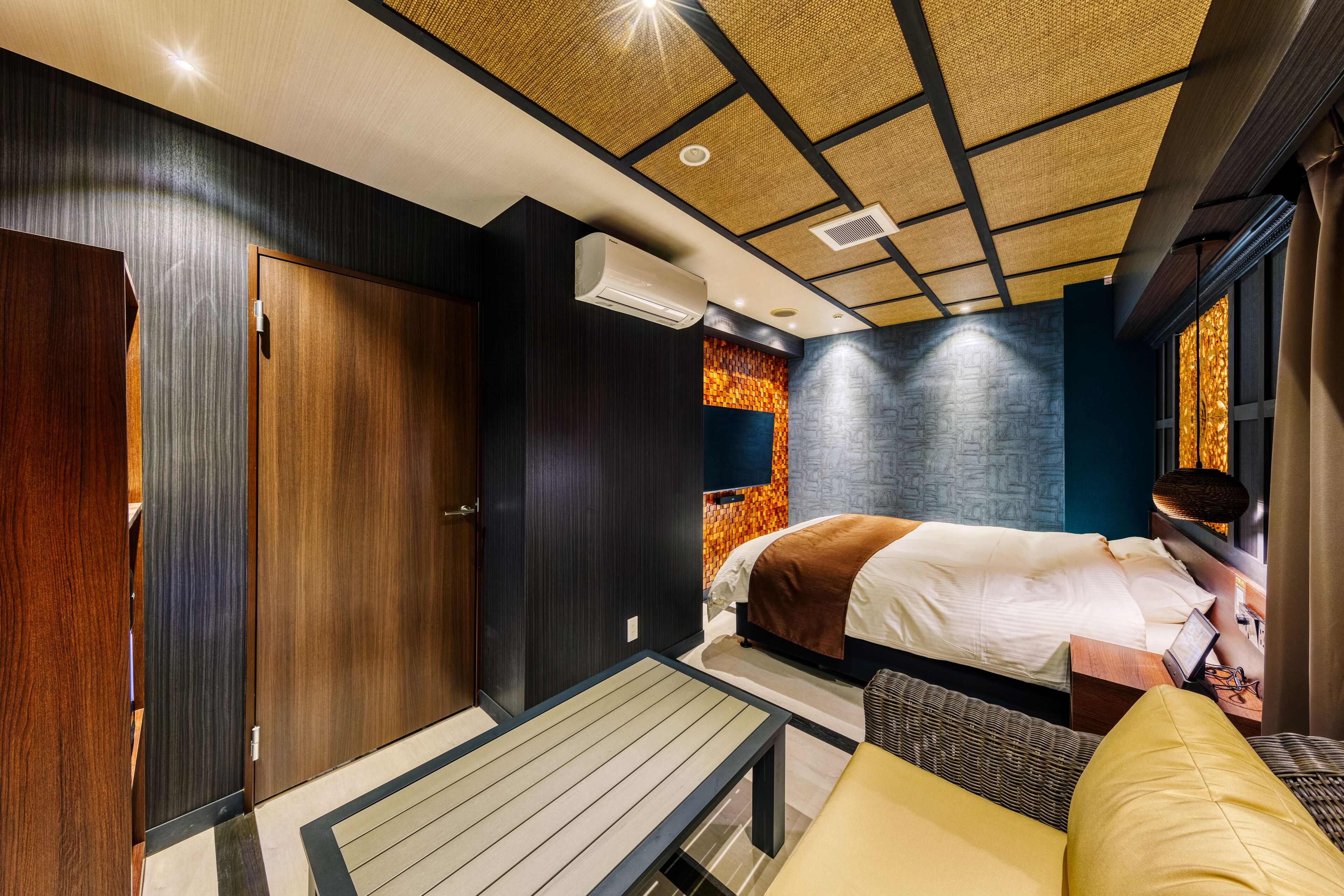 A modern hotel room with a large bed, a small table, a bench, and a wardrobe.