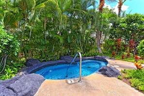 Un bain à remous entouré de plantes tropicales et une piscine à l’eau cristalline.