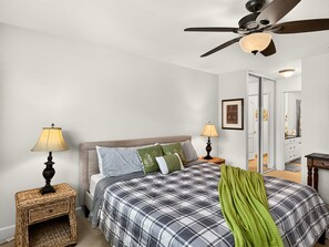 A bedroom with a bed, two bedside lamps, a ceiling fan, and a door leading to a bathroom.