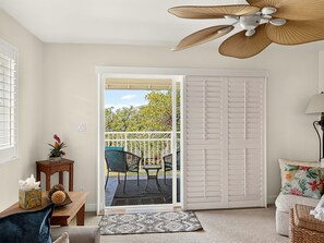 A room with a ceiling fan, a sliding door leading to an outdoor area with chairs and a table, and a small rug on the floor. - Fall Sale Rates - Your Vacation Awaits in Ko Olina KoK-1029B (Kapolei)