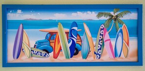 Une œuvre d’art encadrée représentant des planches de surf colorées et un palmier sur une plage.