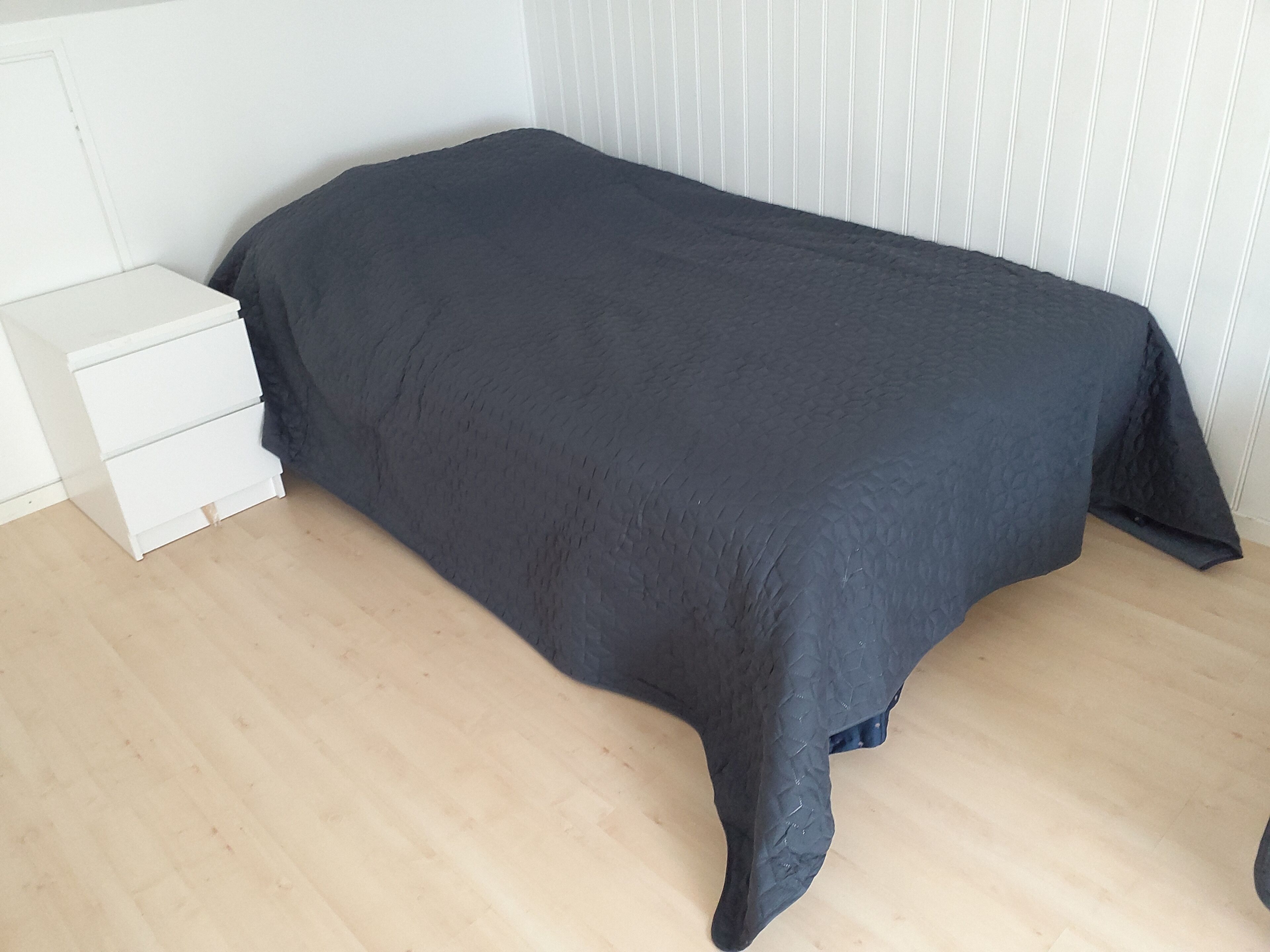Une chambre à coucher avec un lit, une table de chevet blanche et un plancher en bois.