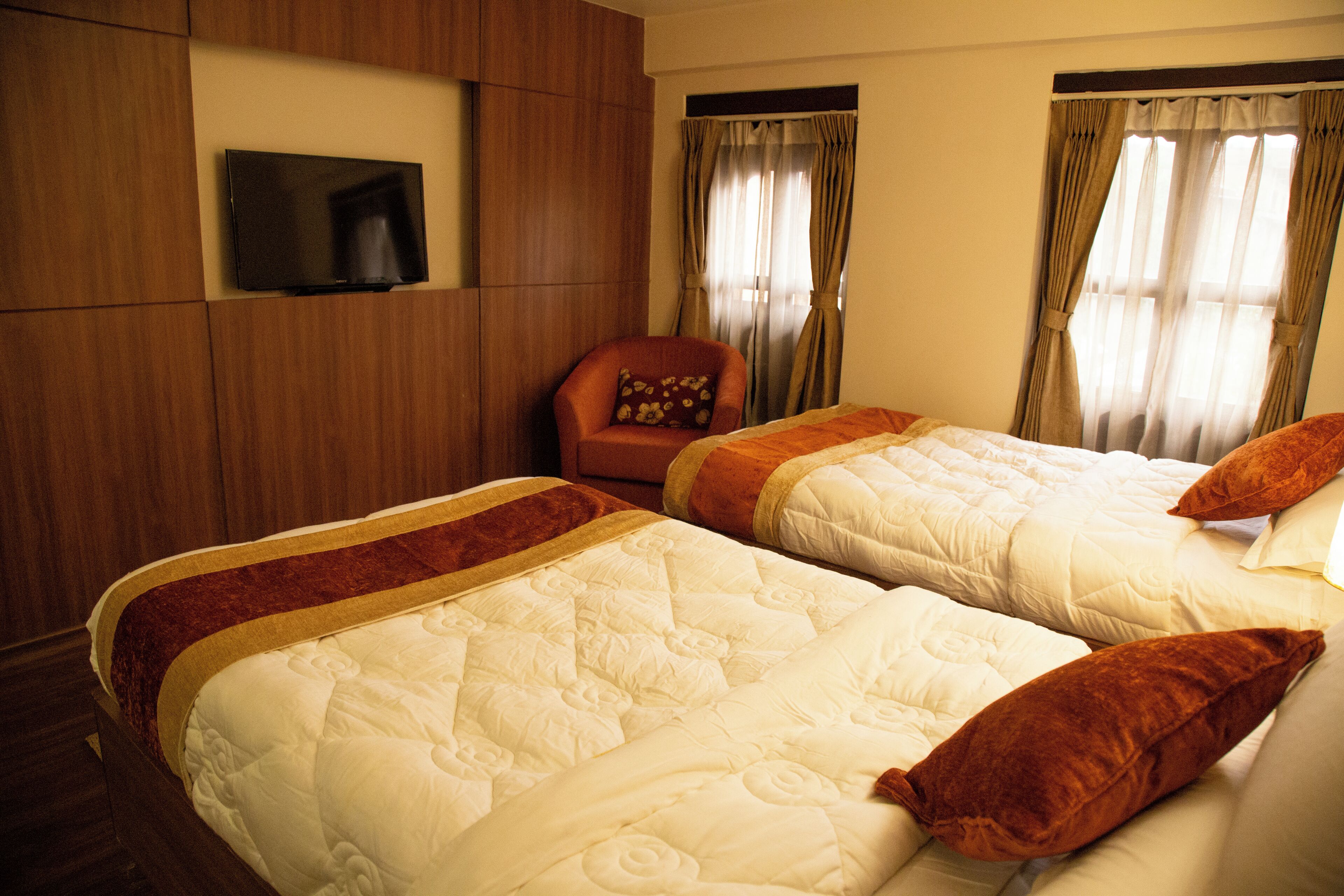 Une chambre d’hôtel avec deux lits, un téléviseur fixé au mur et des rideaux aux fenêtres.
