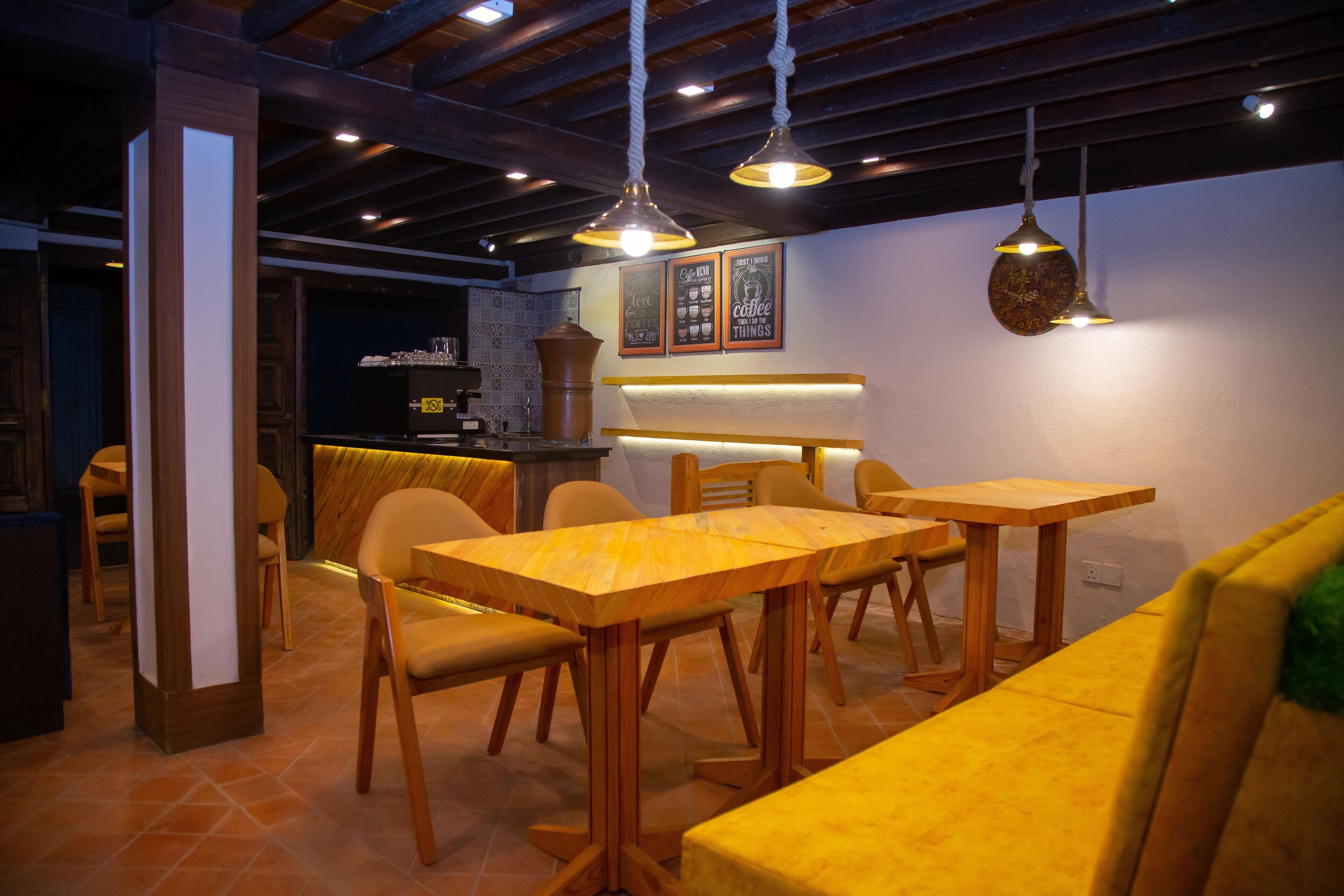 Interior de un restaurante con mesas y sillas de madera, lámparas colgantes y una barra de fondo.