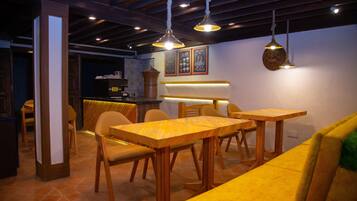 Interior de un restaurante con mesas y sillas de madera, lámparas colgantes y una barra de fondo.