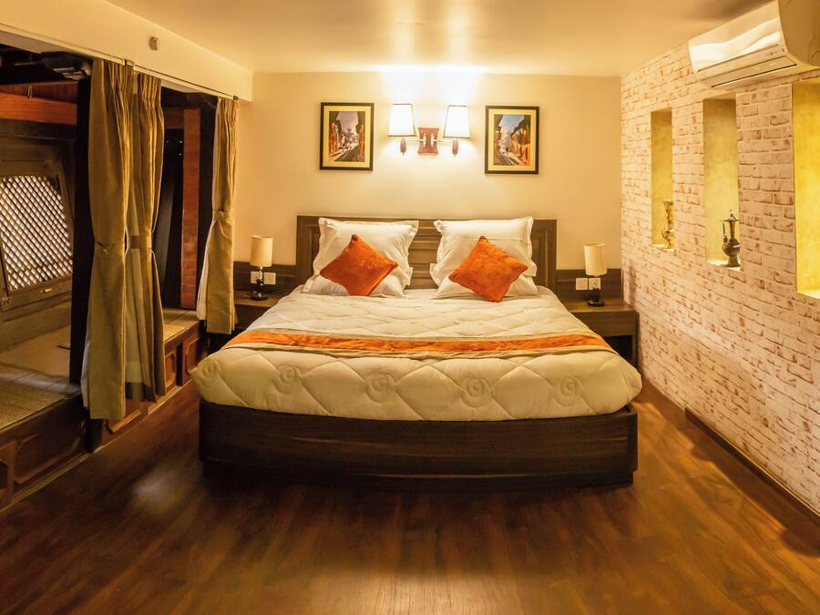 Una habitación de hotel con una cama grande, suelo de madera, pared de ladrillo y una ventana con cortinas.