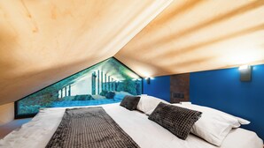 A bedroom with a large bed, a view of trees through a window, and a blue wall. - Ostravinka - Boutique Apartment (Ostrava)