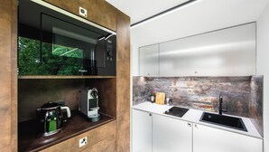 A modern kitchen with a built-in microwave, coffee maker, and a sink with a rustic backsplash. - Ostravinka - Boutique Apartment (Ostrava)