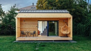 A wooden cabin with a glass door entrance, a small outdoor seating area with chairs, and a grassy lawn. - Ostravinka - Boutique Apartment (Ostrava)