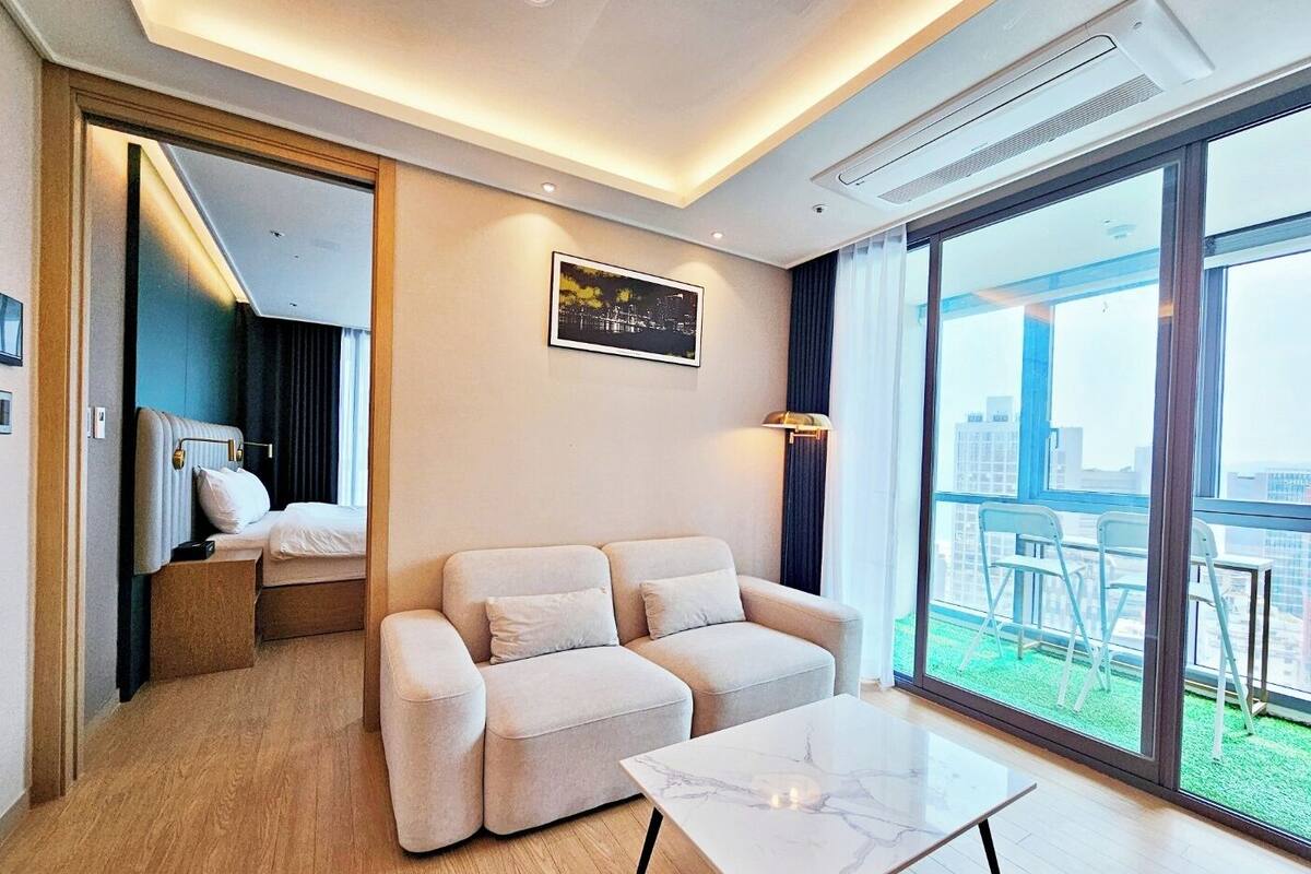 Ein modernes Hotelzimmer mit einer Couch, einem kleinen Tisch und einem großen Fenster mit Blick auf die Stadt.