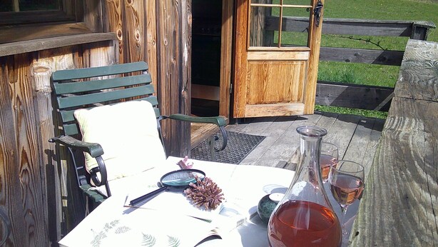 Une terrasse en bois avec une table dressée pour deux personnes, un banc et une porte donnant sur l’extérieur.