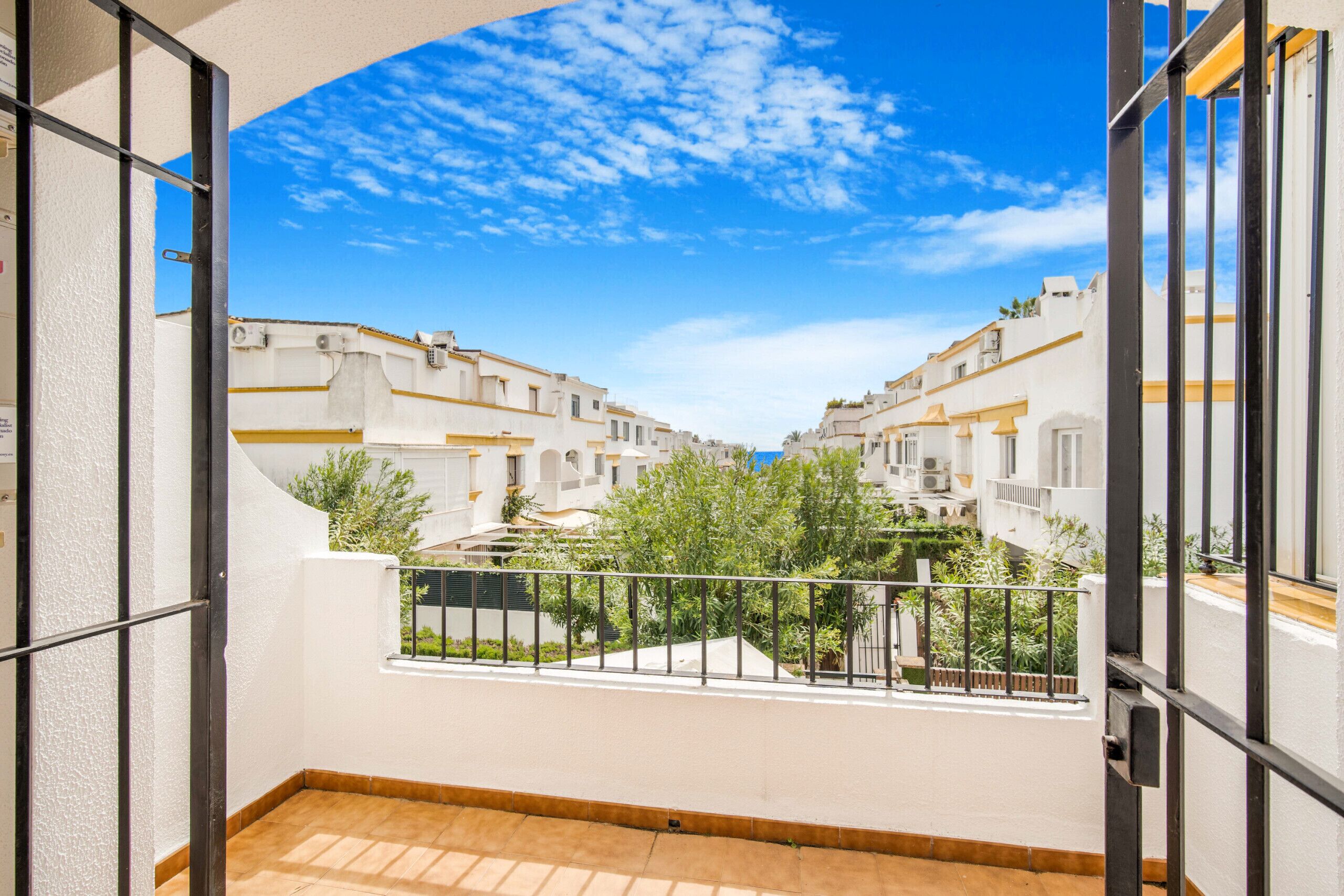A balcony with a view of a residential area, featuring white buildings with balconies and greenery.