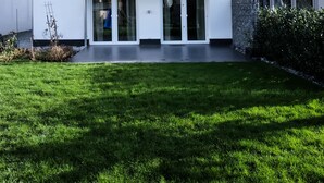 Una moderna casa a due piani con un balcone, ampie porte scorrevoli in vetro e un prato curato.